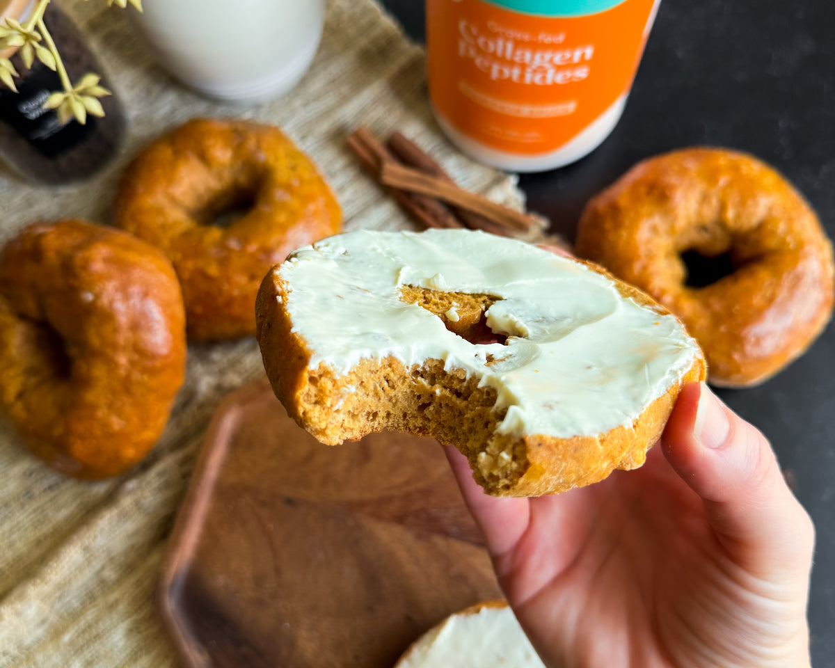 Bagel with cream cheese with other bagels and pumpkin jar in background